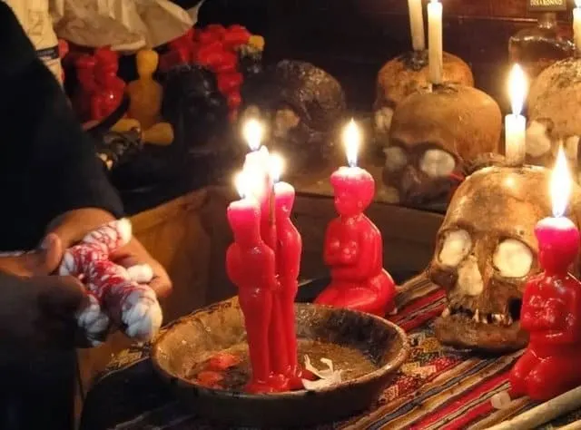 Ritual de amarre con velas rojas en forma de pareja encendidas sobre un plato y un muñeco atado con cordón