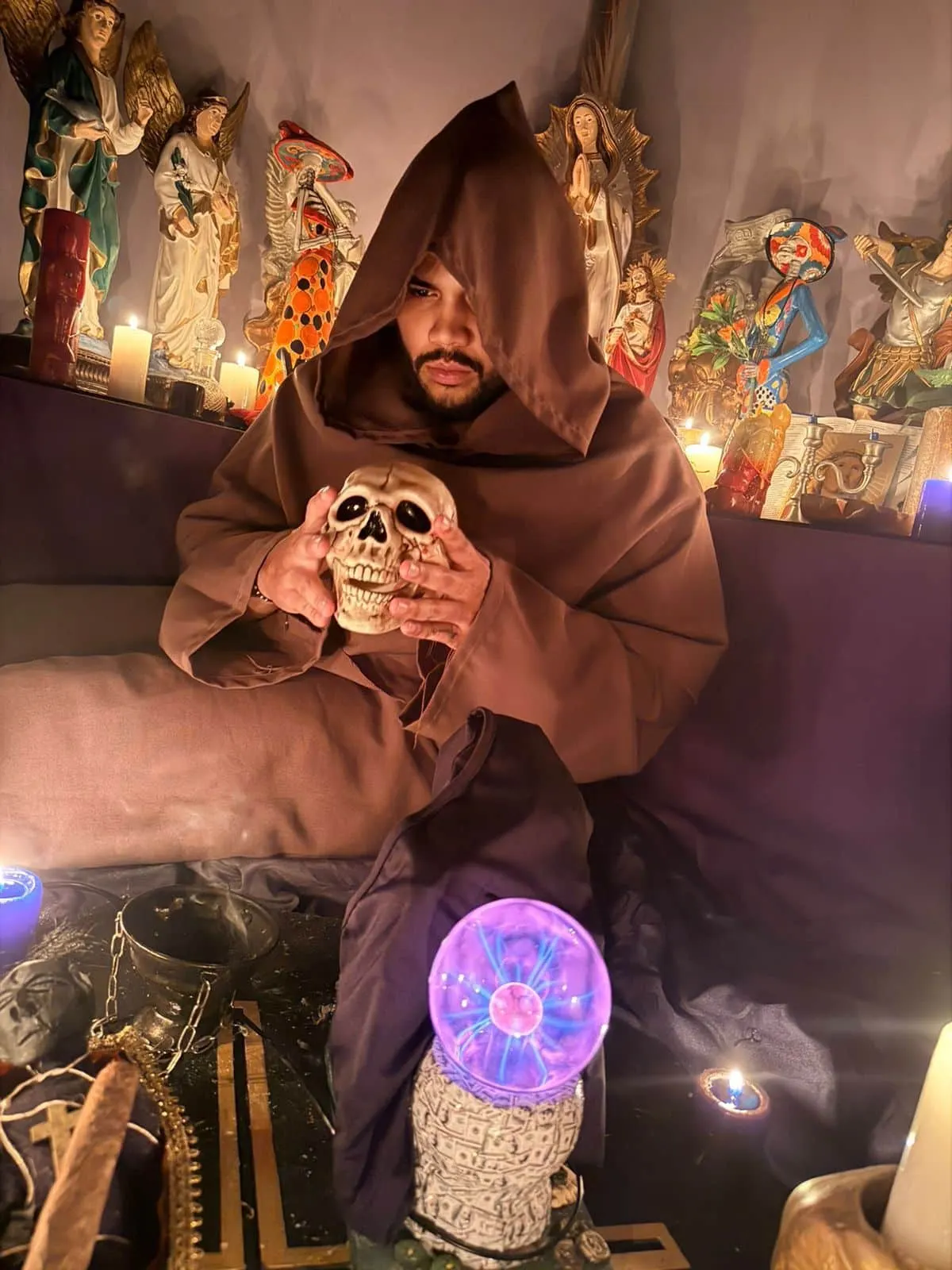 El Maestro Abel con su hábito y capucha sosteniendo una calavera frente al altar con velas encendidas