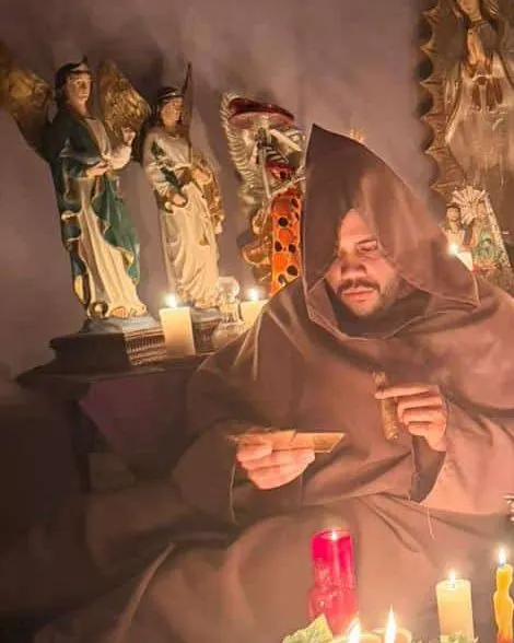 El Maestro Abel leyendo cartas sentado frente al altar, con imágenes de ángeles y velas encendidas