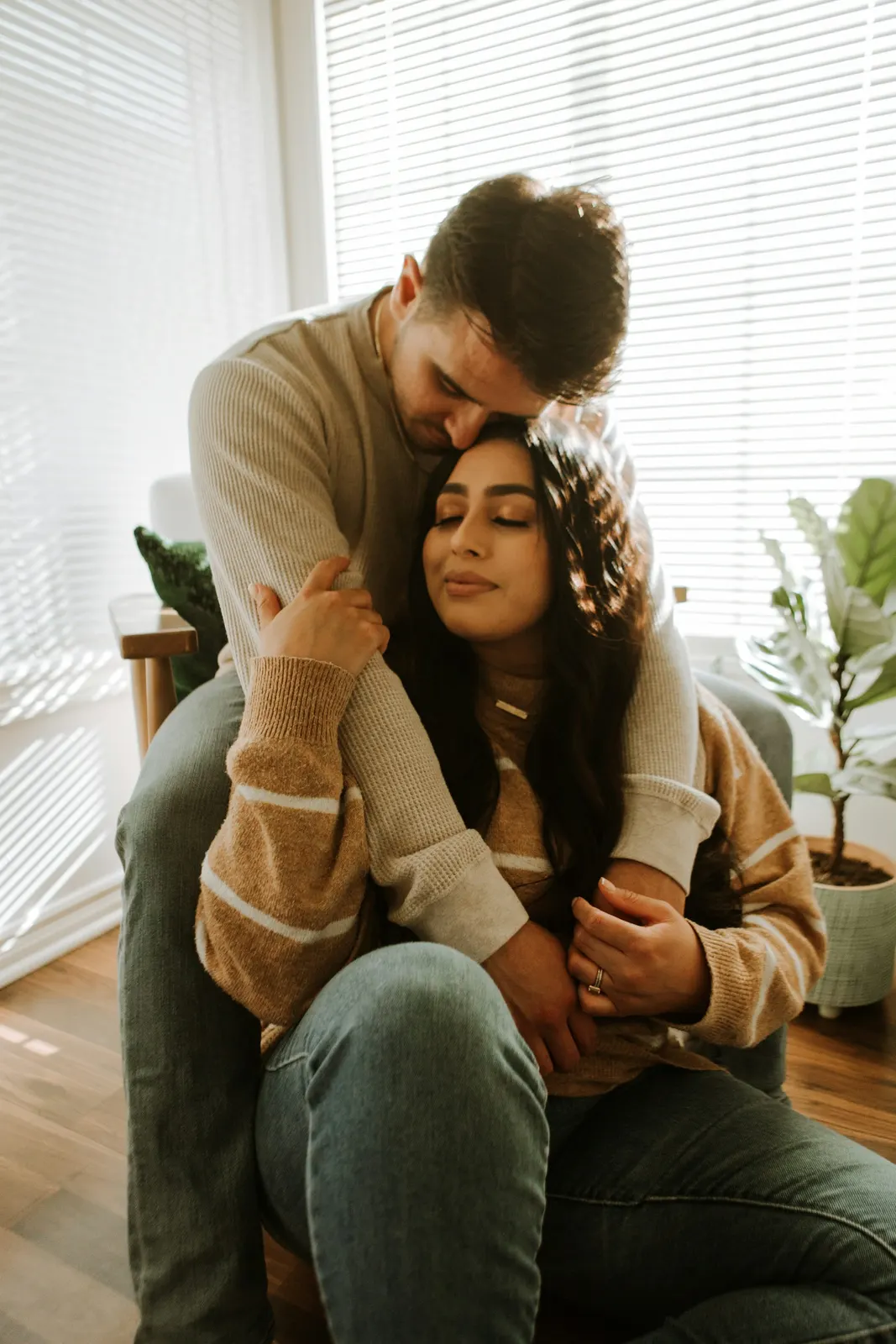 Pareja latina abrazada con ternura en un sillón de su casa