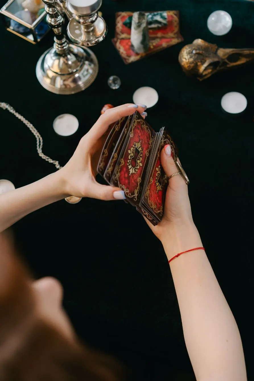 Manos barajando cartas del tarot sobre un paño oscuro con velas y cristales