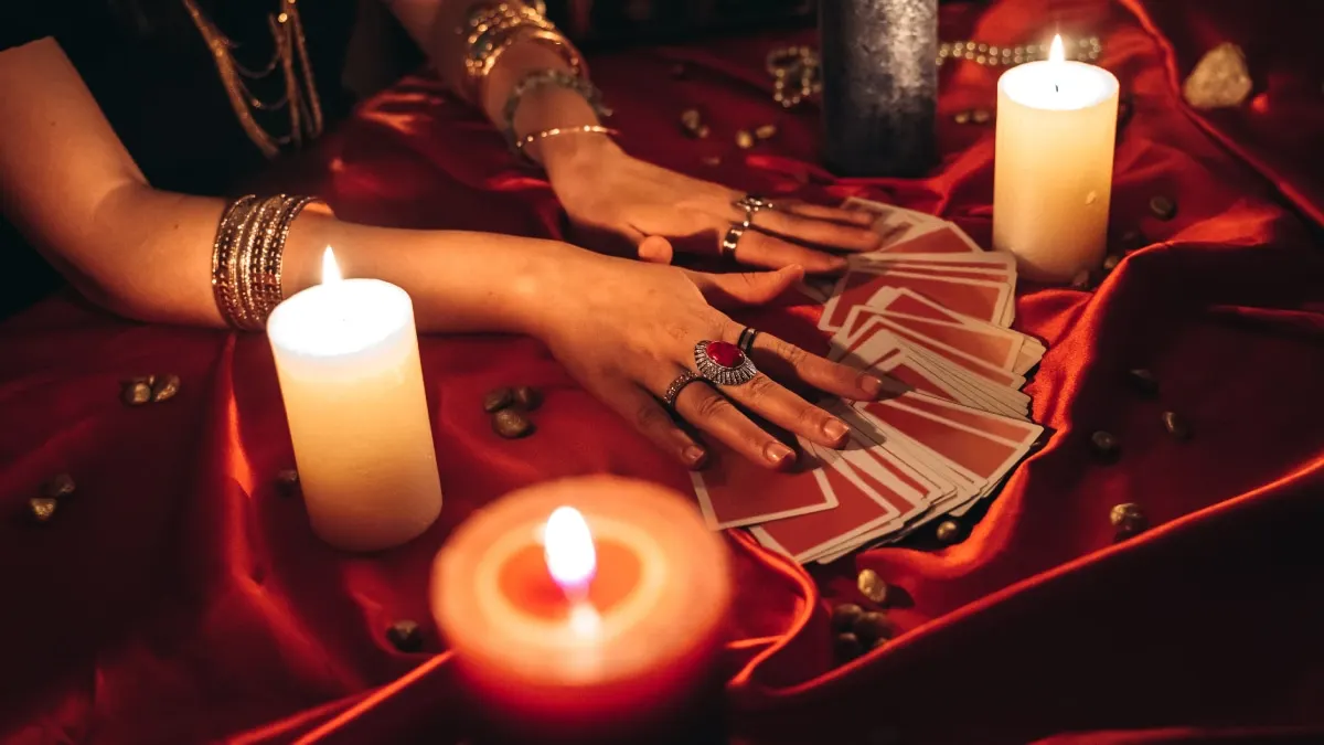Manos extendiendo las cartas del tarot sobre una tela roja junto a velas encendidas